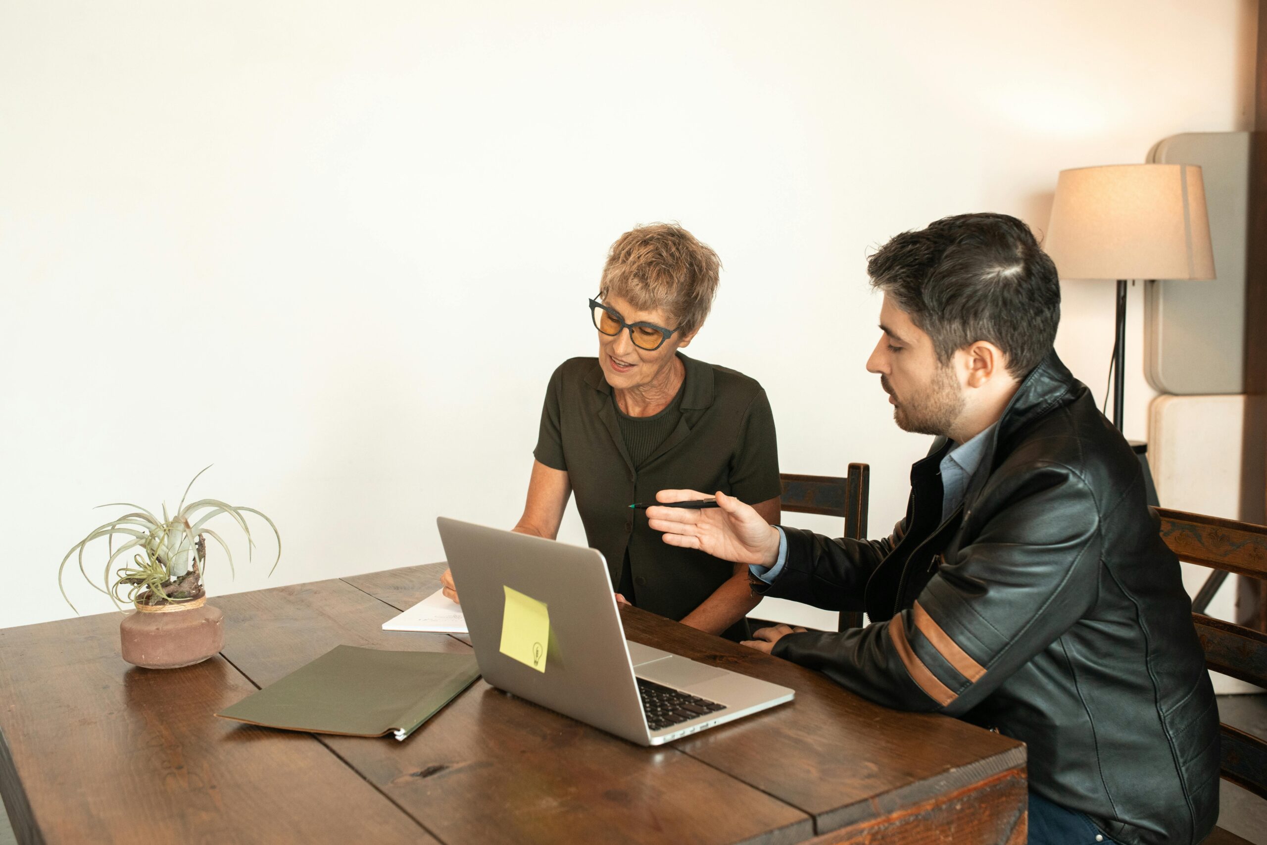 Senior woman and adult man collaborating over a laptop while seated indoors.