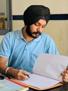 A South Asian man wearing a turban intently studies documents at a desk in India.
